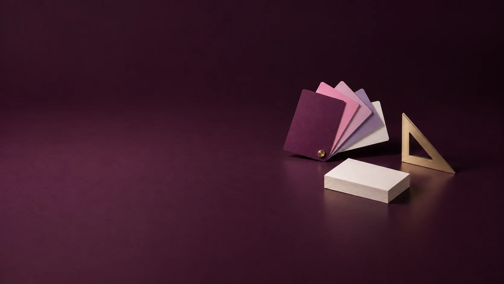 A fan of rose and plum colour cards beside an ivory card stack and metal set square. - Graphic Design & Branding Meta ads research by Madgicx Labs