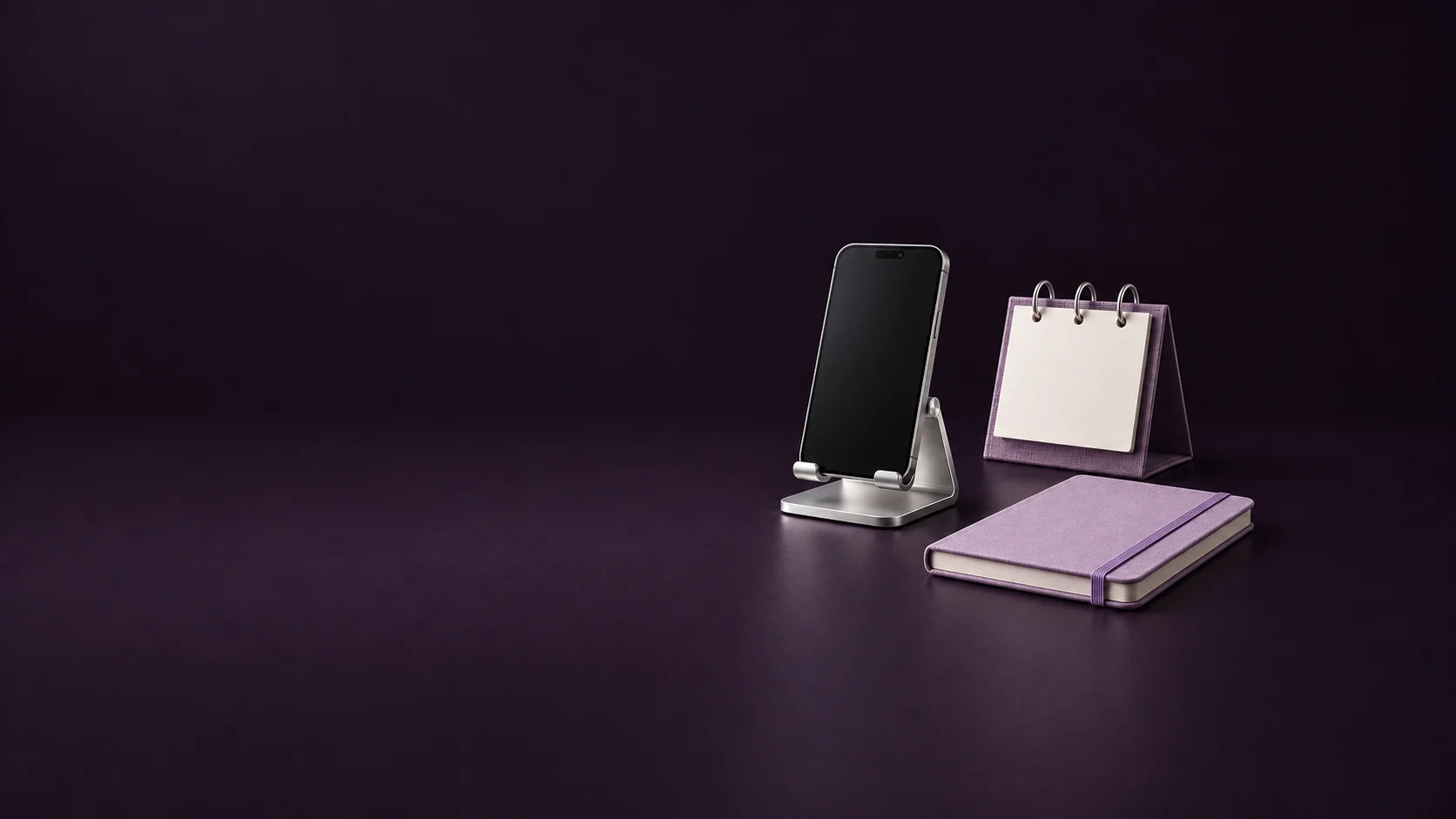 An inactive phone on a silver stand beside a blank violet desk calendar and lavender notebook. - Social Media Marketing Platforms Meta ads research by Madgicx Labs