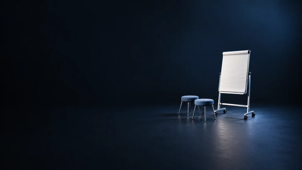 A blank flipchart on a wheeled metal easel beside two blue upholstered stools. - Educational Services & Training Meta ads research index