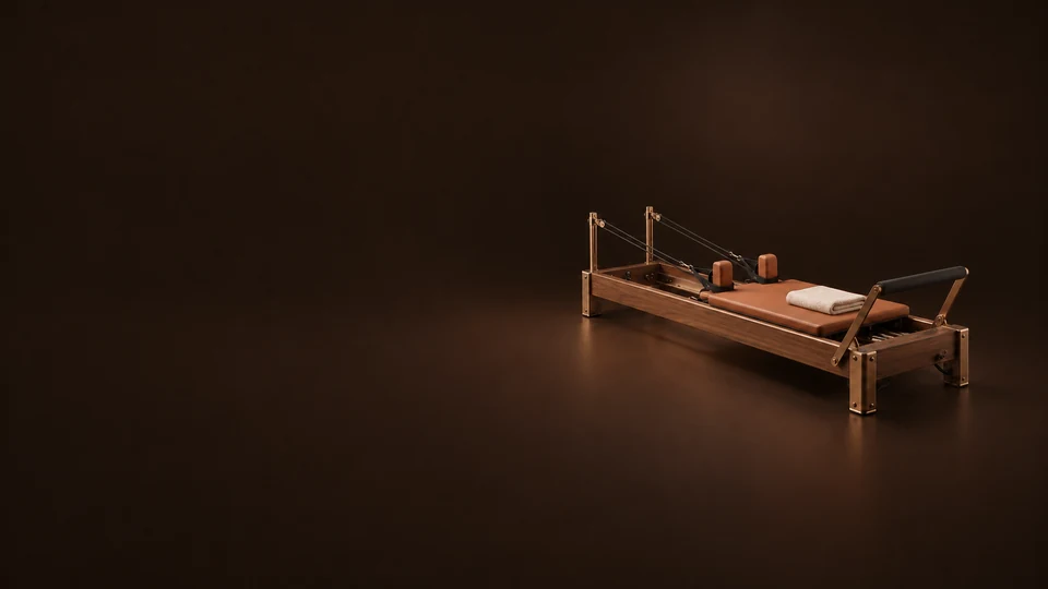 A walnut Pilates reformer with terracotta upholstery, bronze fittings and a folded ivory towel sits on a dark brown floor. - Fitness & Sports Services Meta ads research index