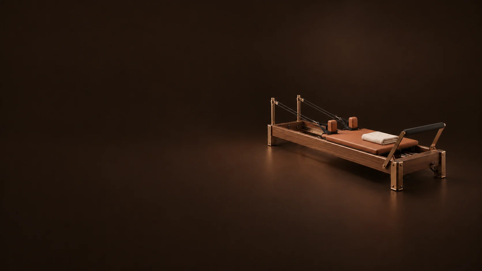 A walnut Pilates reformer with terracotta upholstery, bronze fittings and a folded ivory towel sits on a dark brown floor. - Boutique Fitness Classes Meta ads research by Madgicx Labs