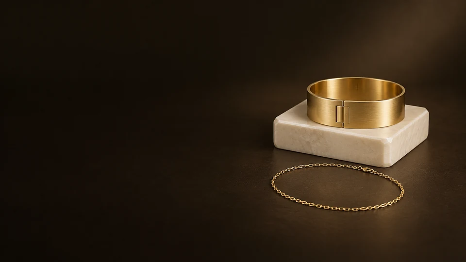 A broad gold-colored cuff on ivory stone with a fine chain loop resting in front. - Jewelry & Accessories Meta ads research index