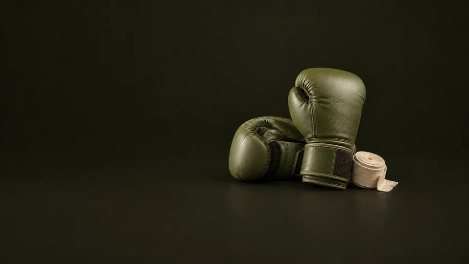 Olive boxing gloves rest with a rolled cream hand wrap on a dark studio floor. - Sports & Outdoor Equipment Meta ads research index