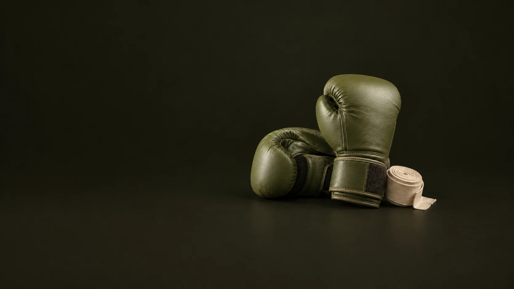 Olive boxing gloves rest with a rolled cream hand wrap on a dark studio floor. - Combat Sports Gear Meta ads research by Madgicx Labs